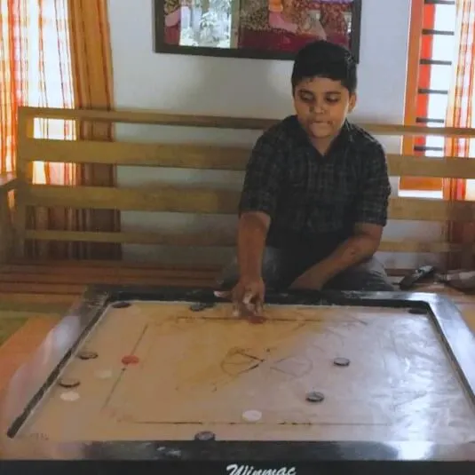 A game of carrom in progress on a carrom board indoors