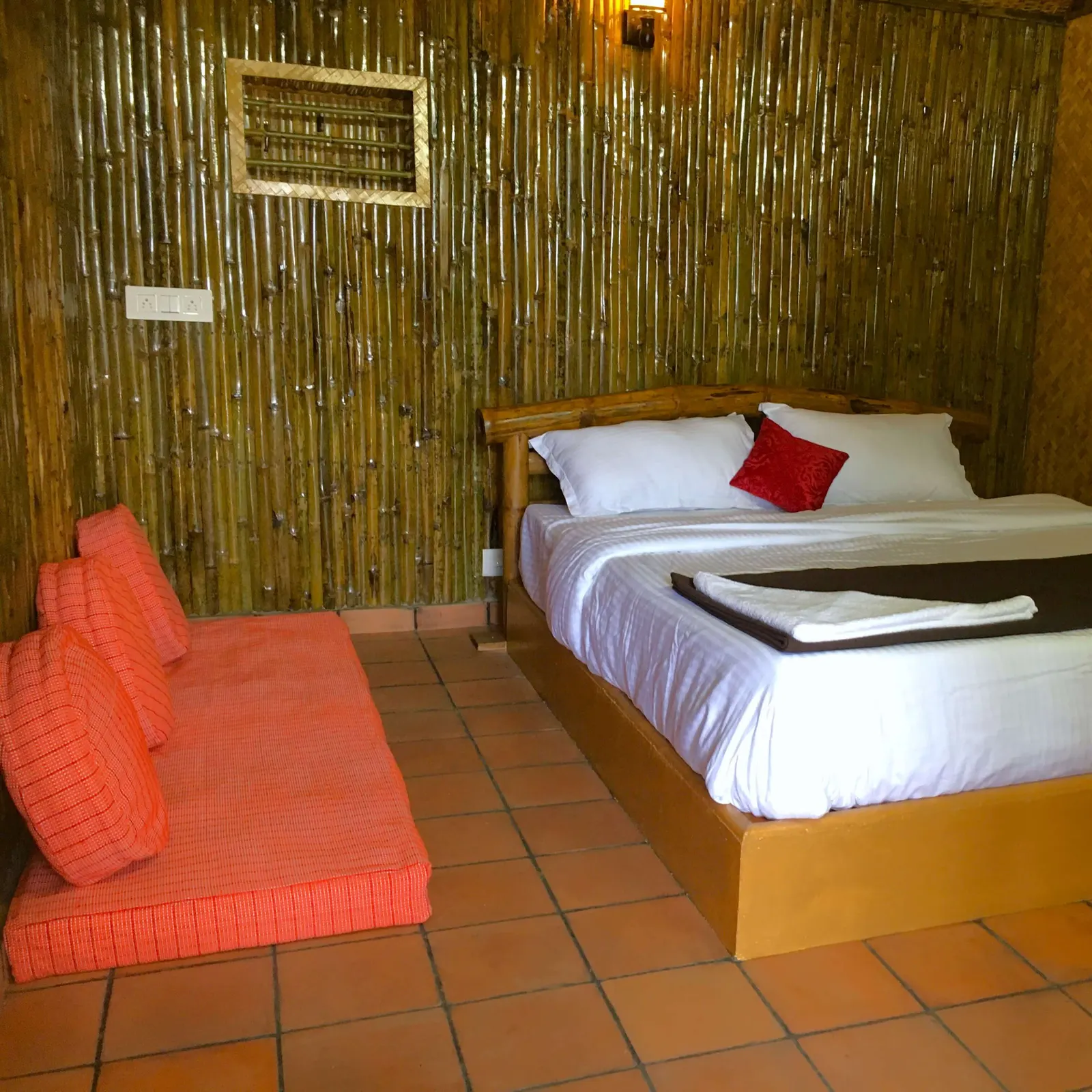 A bamboo-panelled bedroom with a double bed and an orange floor mattress