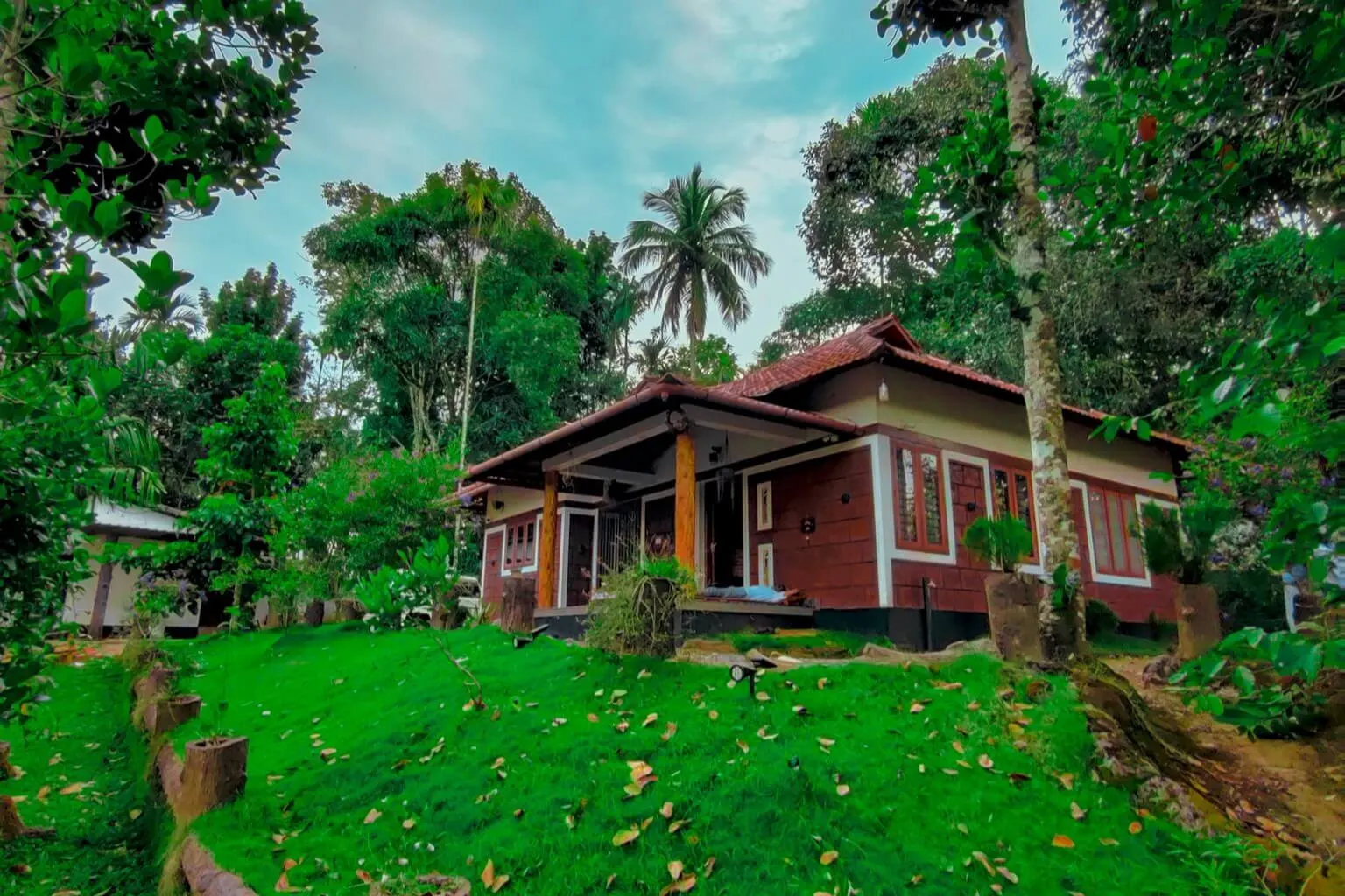 The red-walled villa with its tiled roof and timber-pillared veranda, seen up a grass bank through the trees