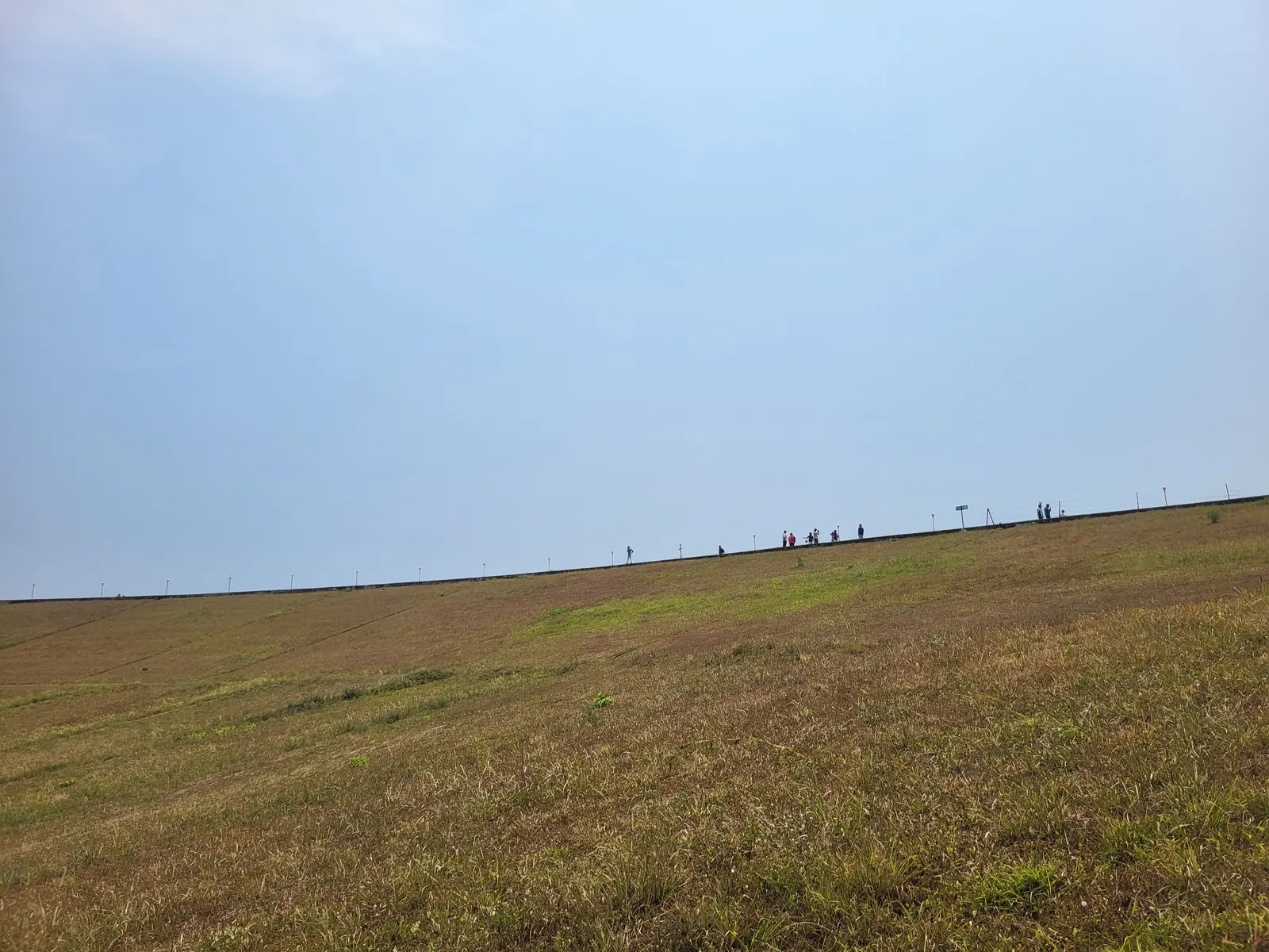 The long grass embankment of Banasura Sagar Dam, with people walking along the crest