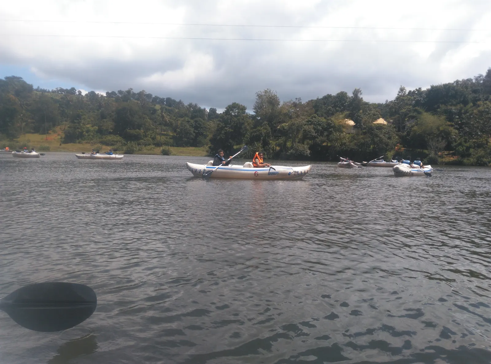 A boat carrying visitors across Karlad Lake, with wooded banks and huts behind