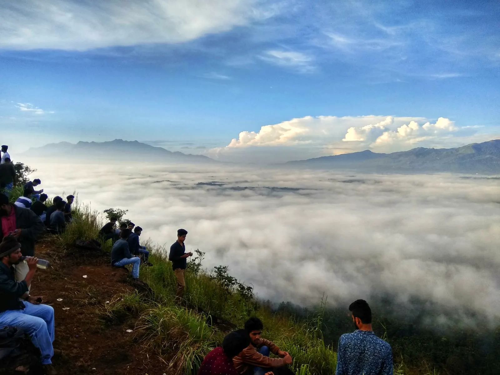 People sitting along the ridge of Kurumbalakotta looking out over a sea of cloud